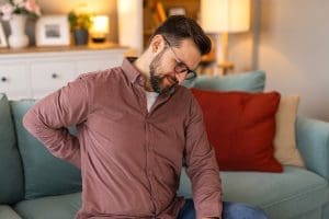 A man with back pain, holding his back on his couch